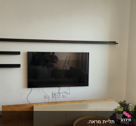 טלוויזיה תלויה על הקיר עם מדפים שחורים